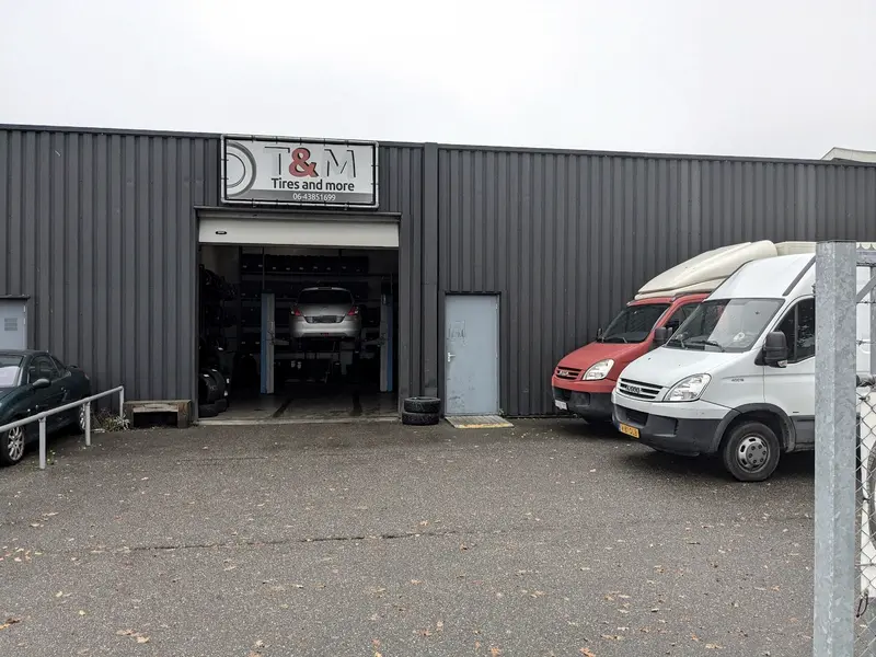 De werkplaats van Tires and More aan de Tussendiepen, met het T&M-bord boven de open deur en een auto op de brug